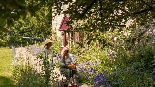 Two women in the garden in front of the Cherryburn museum. One is riding a mobility scooter/